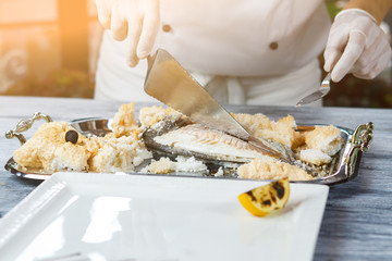 Hand with spatula cutting fish. Tray with cooked fish. Dorado fish prepared by chef. Seafood delicacy in restaurant kitchen.