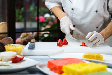 Obraz na płótnie Canvas Hand with knife cuts strawberry. Berries on white cooking board. Fresh ingredients for a dessert. Chef working in the kitchen.