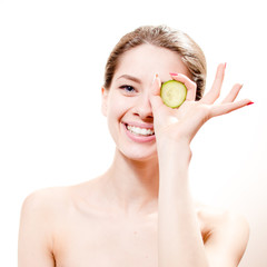 funny spa: young beautiful woman standing with slice of cucumber in the hand one piece on eye isolated on white background, portrait