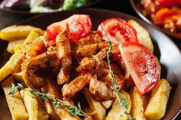 Fried potato with meat and tomato close-up. Serving of clay brown plate with fried potato with meat . Served table with food, focus on portion of fried potato with meat and tomato.