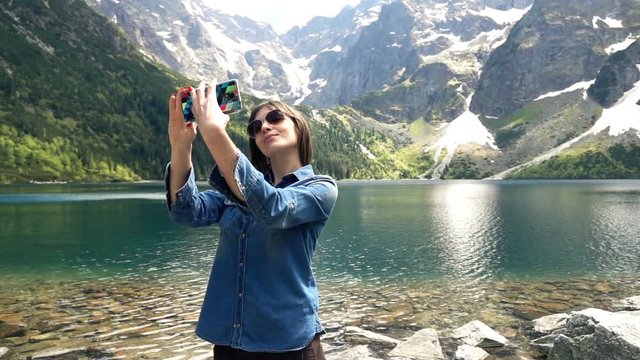 Young woman taking selfie photo by lake and mountains, super slow motion 240fps

