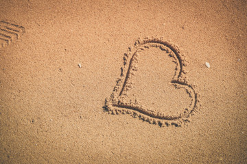 Love heart sign draw on sand background texture. joyful sunny outdoors 