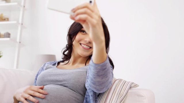 pregnant woman taking selfy by smartphone at home