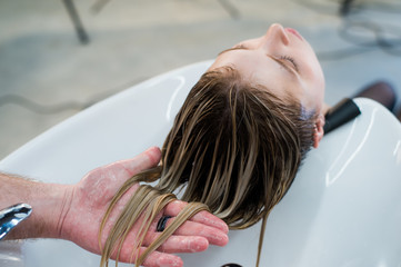 Naklejka premium Hair care in modern spa salon. Male hairdresser washing teen girl's hairs