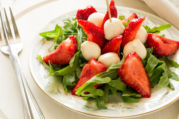 Fresh salad with strawberry, arugula and mozzarella on white plate
