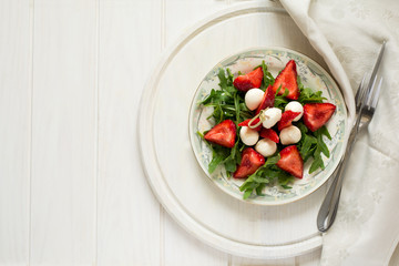 Fresh salad with strawberry, arugula and mozzarella on white plate