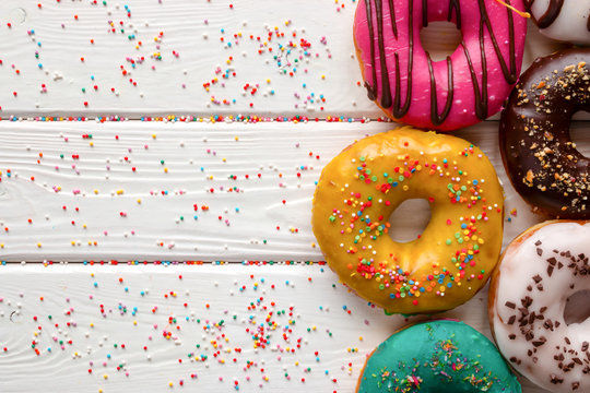 donuts in different glazes on wooden white background and space for text