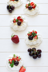 Homemade small pavlova meringue cakes with mascarpone cream, strawberries, cherries and fresh mint leaves on white wooden background