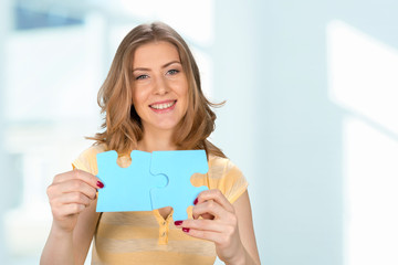 Beautiful young business woman holding a blue puzzle piece