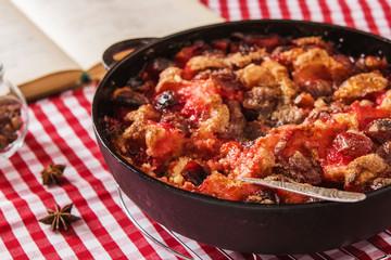 Light summer plums skillet cake on a red tablecloth in a cage with a cookbook and spices 