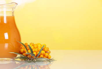 Jug juice from berries sea buckthorn on abstract yellow background.