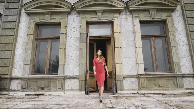 Attractive girl in red dress goes on the balcony of an old manor.