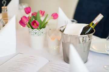 Wino w pojemniku z lodem i różowe kwiaty tulipany zdobiące stół w restauracji - obrazy, fototapety, plakaty