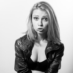 fashion rock star making faces. black and white portrait of mouth open sexy blond young lady in leather jacket posing over light copy space background & looking at camera