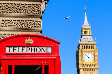 Fototapeta na wymiar Iconic red telephone box with Big Ben and a passing flight against blue sky in the background