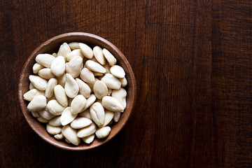 Rustic wooden bowl of peeled whole almonds isolated on dark wood