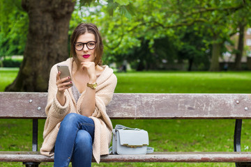 Young woman sitting in the park with phone 