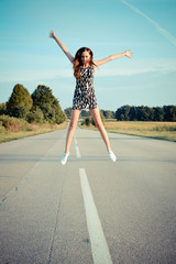 Fototapeta na wymiar road star: portrait of beautiful brunette young woman having fun happy jump on the country road on green summer outdoors copy space background