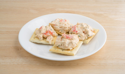 Plate of lobster dip on saltine crackers on a wood table.
