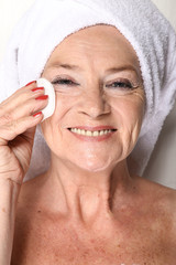 Radosna twarz starszej kobiety z wacikiem i białym ręcznikiem na głowie