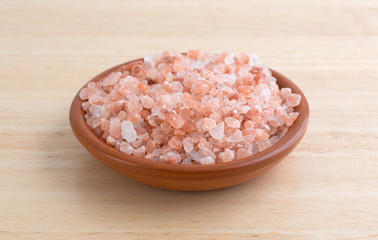 Fototapeta na wymiar Side view of Himalayan pink salt in a small bowl on a wood table.
