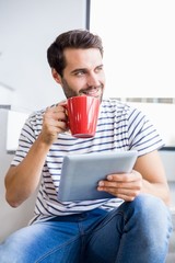 Happy man holding digital tablet while having cup of coffee