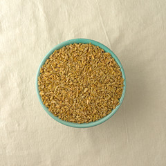 Top view of a bowl of cracked freekeh on a beige tablecloth illuminated with window light.