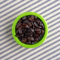 Top view of diced prunes in a green bowl on striped tablecloth.