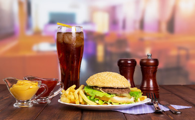 Hamburger, french fries, glass cola, sauces, spices on background cafe.