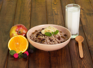 Bowl oatmeal with raisins, fruit, glass milk and spoon.