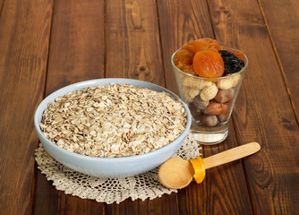 Bowl oatmeal, dried fruit, nuts, spoon on dark wooden background.