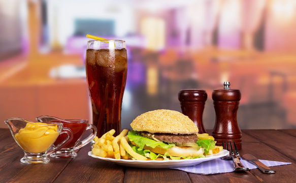 Hamburger, french fries, glass cola, sauces, spices on background cafe.