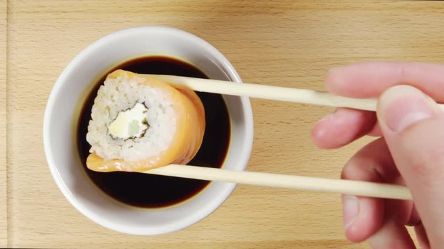 TOP VIEW: Human hand dips a sushi by chopsticks in a soy sauce cup