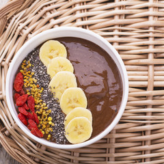 bowl of breakfast with chocolate banana smoothies garnished  bee pollen, chia seeds, goji berries and  on  wooden background