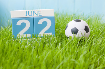 June 22nd. Image of june 22 wooden color calendar on green grass background with football outfit. Summer day