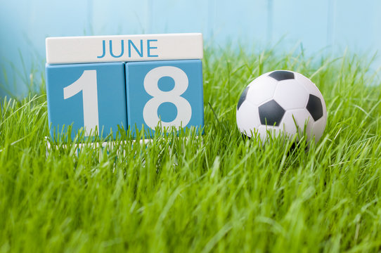 June 18th. Image of june 18 wooden color calendar on green grass background with football outfit. Summer day