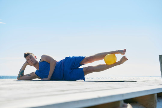 Man on pier lying on side resting on elbow, ball between legs