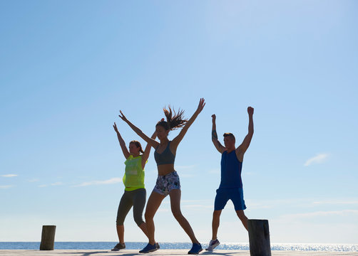 Friends on pier wearing exercise clothes arms raised exercising
