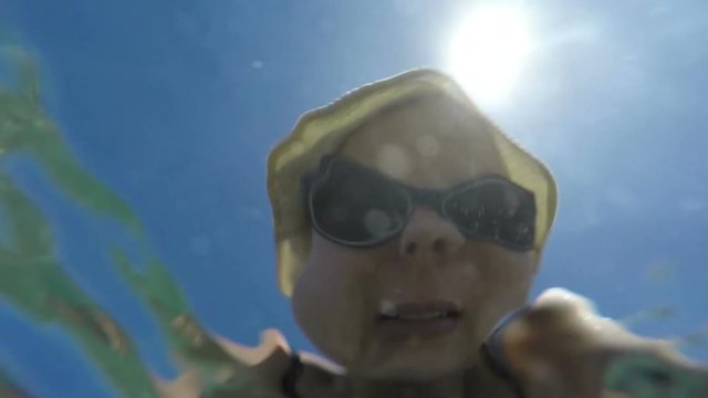 Underwater slow motion view of a woman face in hat and sunglasses through the water surface.