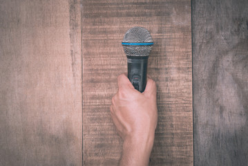 Hand holding a microphone on wooden background