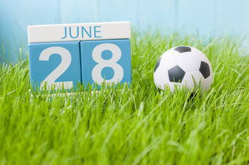 June 28th. Image of june 28 wooden color calendar on green grass background with football outfit. Summer day