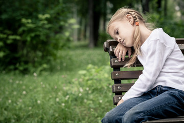 Portrait of sad blond little girl sitting on bench