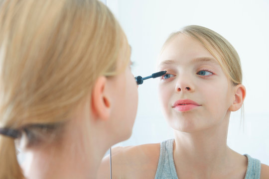 Over the shoulder mirror image of girl applying mascara