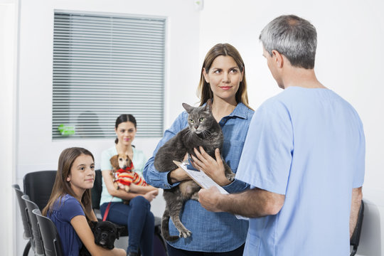 Woman Carrying Cat While Looking At Nurse In Clinic