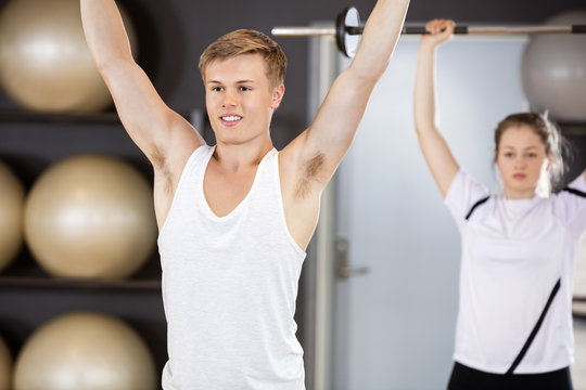Man Exercising With Woman In Background At Gym