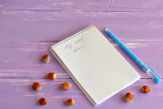 Paper notebook, pen, nuts on lilac wooden background. My diet plan. Slimming concept. Lifestyle. A notepad diet menu. Notepad for diets programs