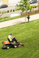 utility workers of municipality  with  brush cutting  and   lawn  mower , riding  mower,  in city park ; selective focus