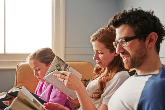 Mid adult parents and daughter on sofa on reading books