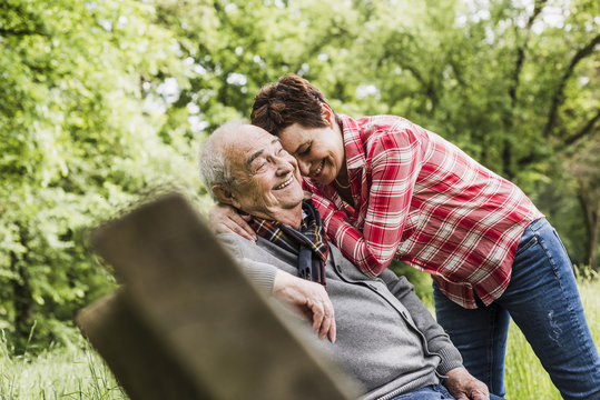 Happy woman hugging her old father sitting on a bench in nature