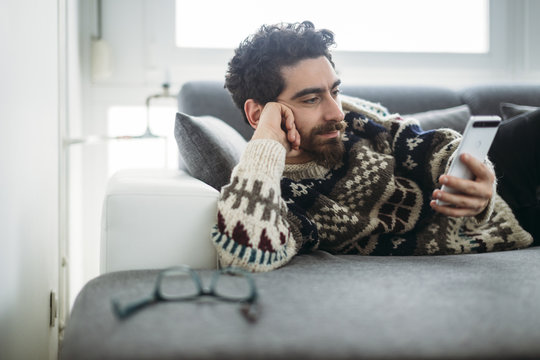 Man lying on a couch looking at phablet